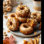 “Glazed baked pumpkin donuts stacked on a fall-themed platter with chopped walnuts and coffee on the side”